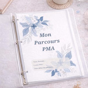 Peut inclure: Un classeur transparent ouvert, affichant une page avec le texte "Mon Parcours PMA" et des illustrations florales bleues. On aperçoit également une tasse de café, des lunettes et une pince dorée.