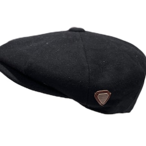 Könnte beinhalten: Eine schwarze Wollmütze im Newsboy-Stil mit einem braunen Lederpatch, auf dem "The Flat Cap Co." steht.