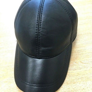 May include: A black leather baseball cap with a curved peak. The cap features a button on the crown and stitched detailing. The hat is made from a smooth, shiny leather.