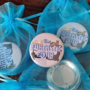 Op de afbeelding: Drie blauwe organza zakjes met witte knopen met een kattenontwerp en de tekst "The FurTastic Four".