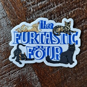 May include: A white sticker with blue lettering that reads "The Fur-tastic Four". The sticker features four cartoon cats in different poses.