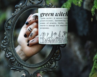 May include: White ceramic mug with a black outline of flowers and the text "green witch (grēn wiCH): A nature-loving practitioner, harnessing the power of plants, herbs, and earth's energy for magical purposes."