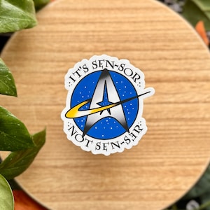 May include: A white sticker with a blue and yellow starfleet logo. The text around the logo reads "It's Sen-sor. Not Sen-sir."