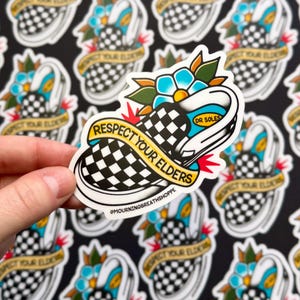 K&ouml;nnte beinhalten: Ein gestanzter Aufkleber mit einem schwarz-wei&szlig; karierten Slipper, einer blauen Blume und gr&uuml;nen Bl&auml;ttern. Ein gelbes Banner &uuml;ber dem Schuh tr&auml;gt den schwarzen Schriftzug RESPECT YOUR ELDERS. Zudem sind DR SOLES und @MOURNINGBREATHSHOPPE aufgedruckt.