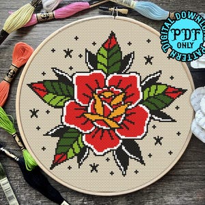 May include: A cross-stitch pattern of a red rose with green leaves and yellow center, surrounded by small white stars on a beige background. The pattern is in a round embroidery hoop.