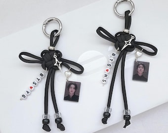 May include: Two black cord keychains featuring intricate knots, silver metal rings, and star-shaped charms. Each keychain includes white letter beads spelling BTS YG or BTS HS, a small red heart bead, a silver heart charm, and a rectangular photo pendant.