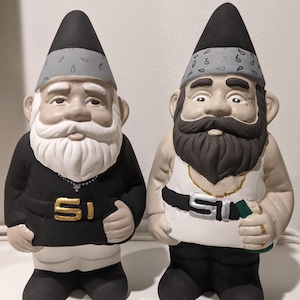 May include: Two garden gnomes with black and white clothing and gray bandanas. The gnome on the left has a white beard and a gold chain necklace with the letter 'SI' on it. The gnome on the right has a black beard and a gold chain necklace with the letter 'SI' on it.