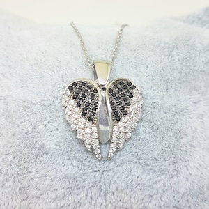 Puede incluir: Collar de plata con un colgante en forma de corazón con alas de cristal negras y blancas.