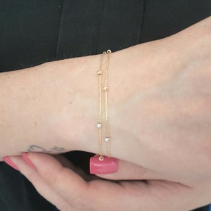 May include: A delicate gold bracelet with two strands, adorned with small, evenly spaced beads. The bracelet features a mix of gold, rose gold, and silver-toned beads. The jewelry is displayed on a wrist.