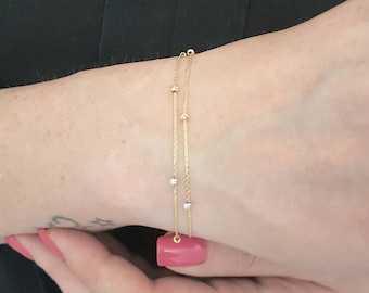 May include: A delicate gold bracelet with two strands, adorned with small, evenly spaced beads. The bracelet features a mix of gold, rose gold, and silver-toned beads. The jewelry is displayed on a wrist.