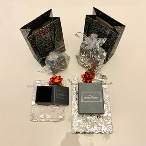 May include: Two black gift bags with silver floral patterns, two small black gift boxes with red bows, and two silver gift bags with red bows and black boxes with the text "Latika Jewelry" on them.