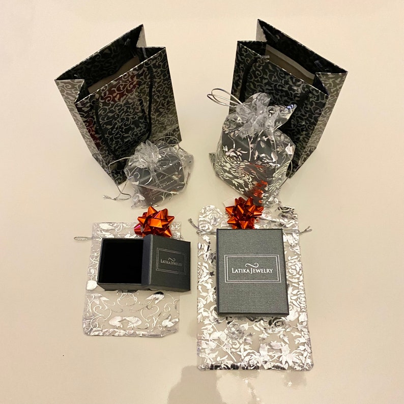 May include: Two black gift bags with silver floral patterns, two small black gift boxes with red bows, and two silver gift bags with red bows and black boxes with the text "Latika Jewelry".