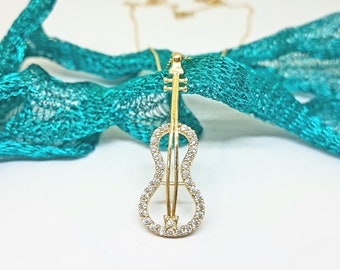 May include: A gold necklace with a pendant shaped like a violin. The violin is decorated with small, clear stones.