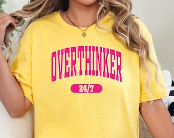 May include: Yellow t-shirt with the word "OVERTHINKER" in pink block letters and "24/7" in a pink oval. The shirt is a casual style, with a relaxed fit.