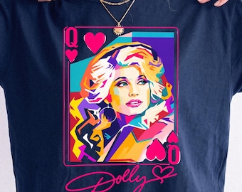 May include: A navy blue short-sleeve t-shirt featuring a colorful pop art graphic of a woman with blonde hair styled as a playing card queen. The design includes pink heart symbols, the letter Q, and the cursive text Dolly written in bright pink.