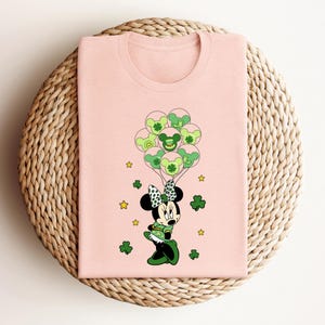 a pink shirt with a mickey mouse holding shamrocks
