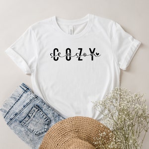 May include: White t-shirt with black text that reads "Cozy season" with a small heart symbol.