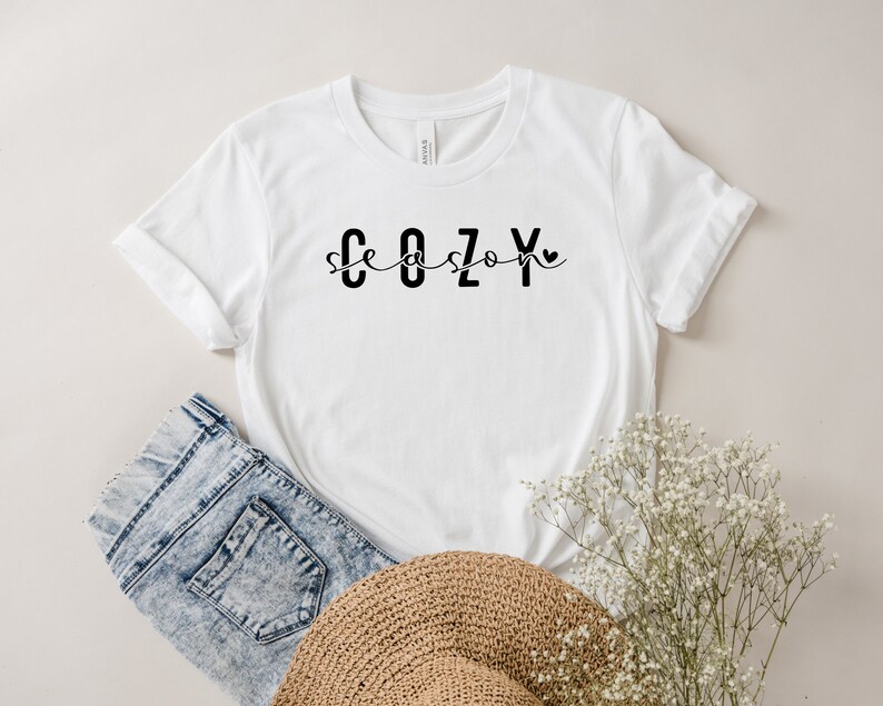 May include: White t-shirt with black text that reads "Cozy season" with a small heart symbol.