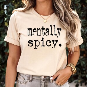 May include: A beige t-shirt with the text "mentally spicy." printed in black.