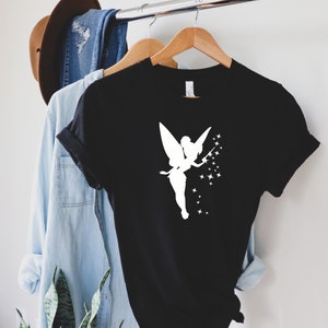 Puede incluir: Camiseta negra con una silueta blanca de un hada con una varita y estrellas.