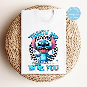 May include: White unisex t-shirt featuring a cartoon character with blue fur, large ears, and an open mouth. The text "TOUCH ME" and "AND I WILL BITE YOU" are in blue, with a black and white checkered circle behind the character.