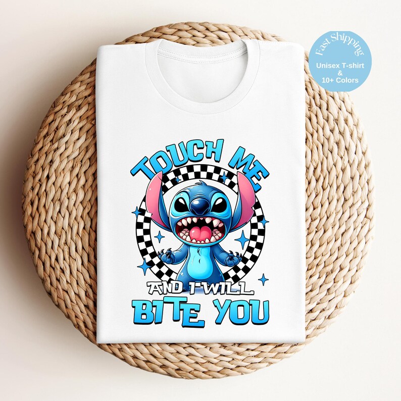 May include: White unisex t-shirt featuring a cartoon character with blue fur, large ears, and an open mouth. The text "TOUCH ME" and "AND I WILL BITE YOU" are in blue, with a black and white checkered circle behind the character.