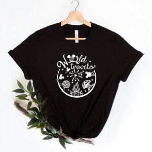 May include: Black t-shirt with a white graphic design. The design features the words "World traveler" in a circular arrangement with iconic travel-themed illustrations, including a castle, fireworks, and a globe.