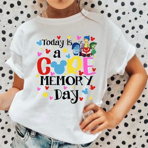 May include: White t-shirt with a colorful graphic that says "Today is a CORE MEMORY Day" with cartoon characters from the movie Inside Out. The graphic also includes Mickey Mouse ears.