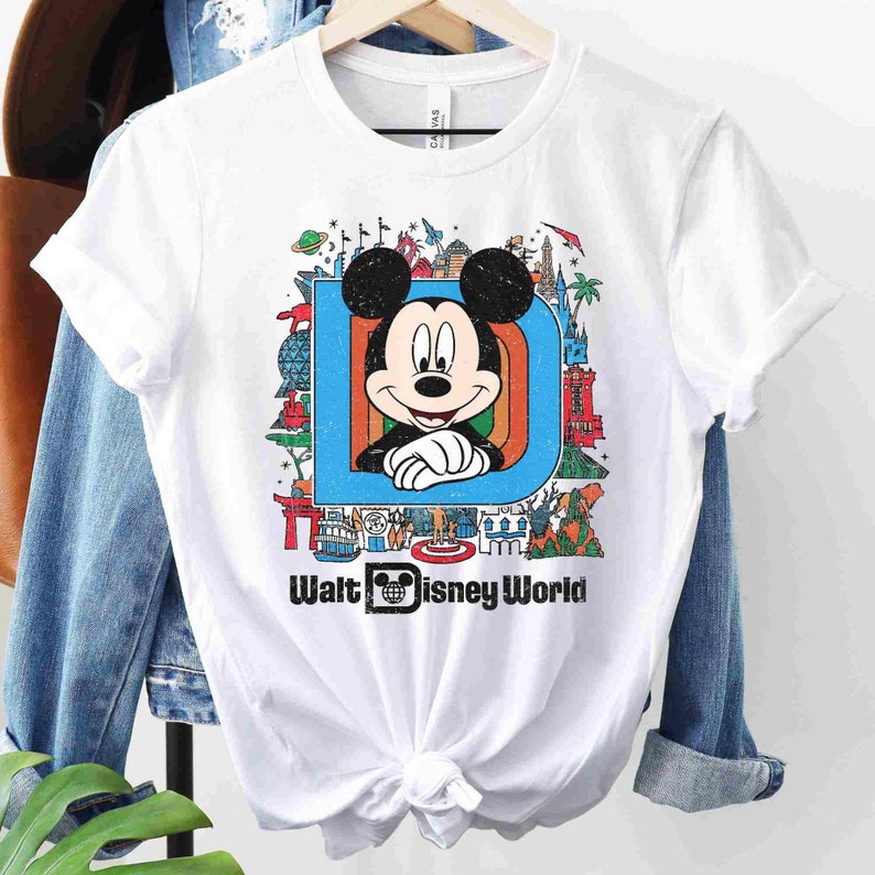 May include: White t-shirt with a colorful graphic of Mickey Mouse in front of the letter "D" with various Disney World attractions. The text "Walt Disney World" is printed below the graphic.