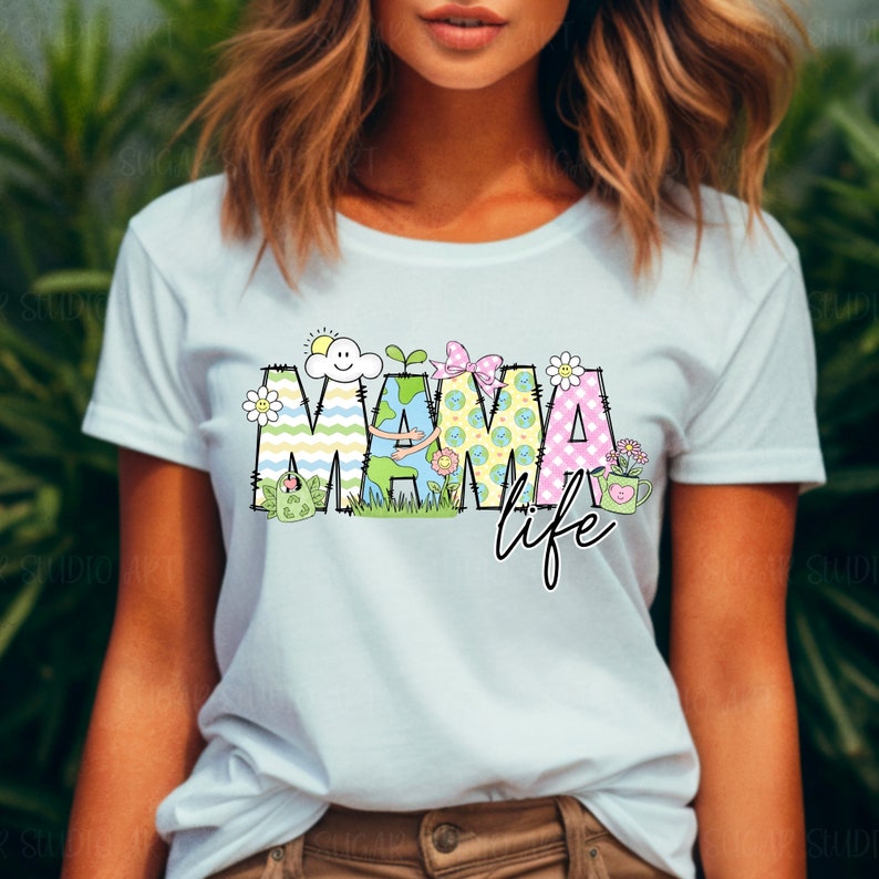 May include: A light blue t-shirt with a colorful graphic design that says "Mama Life". The graphic features a stylized earth with a smiling sun and a green plant.