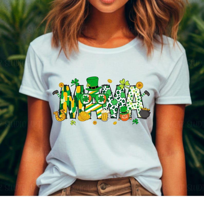 Puede incluir: Camiseta blanca con un gr&aacute;fico verde, amarillo y dorado que dice "MAMA" con tr&eacute;boles, duendes y otras im&aacute;genes con tem&aacute;tica del D&iacute;a de San Patricio.