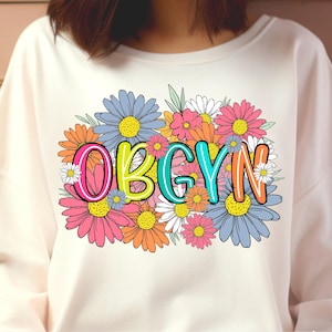 May include: White sweatshirt with a floral design and the word "OBGYN" in colorful letters.