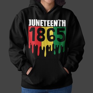 Pu&ograve; includere: Felpa con cappuccio nera con una stampa grafica bianca che dice "Juneteenth 1865". I numeri sono in un design a blocchi di colore rosso, giallo e verde con vernice che cola.