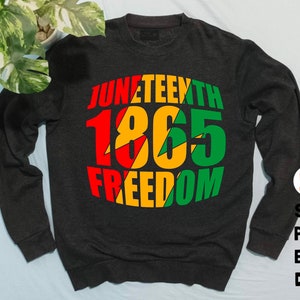 May include: A dark grey sweatshirt with a red, yellow and green graphic design that says "Juneteenth 1865 Freedom".