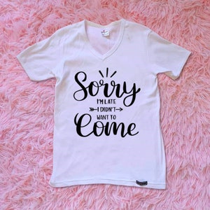 May include: White v-neck t-shirt with black text that reads "Sorry I'm late - I didn't want to come".