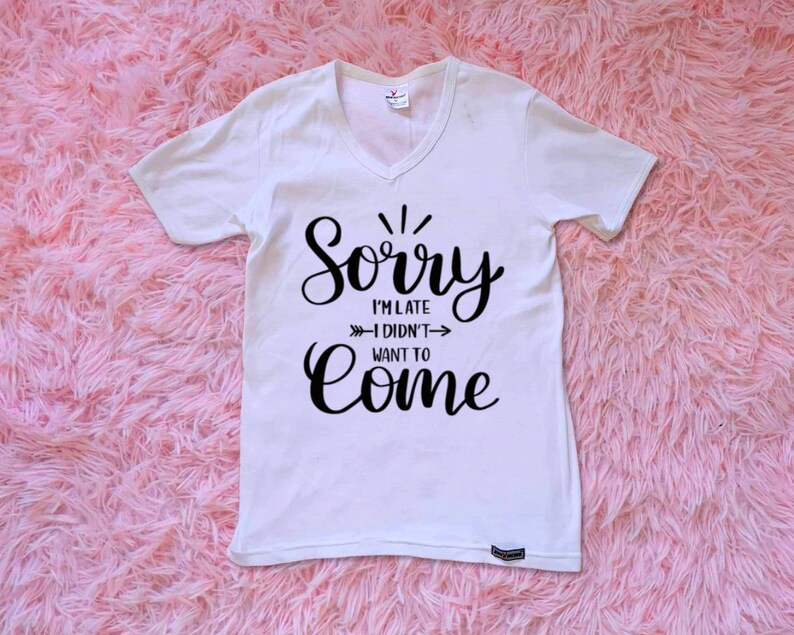 May include: White v-neck t-shirt with black text that reads "Sorry I'm late - I didn't want to come".