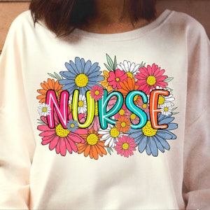 May include: A white sweatshirt with a colorful floral design and the word "NURSE" in the center. The flowers are in shades of pink, blue, yellow, and orange.