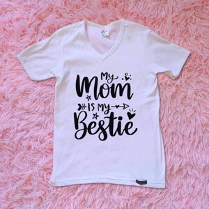 Op de afbeelding: Wit T-shirt met zwarte tekst die "My Mom is my Bestie" zegt met een hart en pijlen.