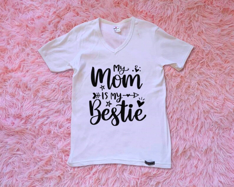 Op de afbeelding: Wit T-shirt met zwarte tekst die "My Mom is my Bestie" zegt met een hart en pijlen.