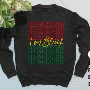 May include: A dark gray sweatshirt with the text "HISTORY" repeated in red, yellow, and green, and the text "I am Black" in yellow cursive.