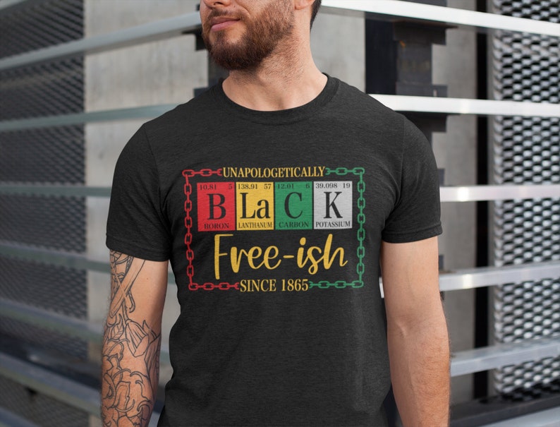 Pu&ograve; includere: Una maglietta nera con un design grafico che presenta la parola "Black" scritta usando simboli di elementi chimici. La grafica include anche il testo "Free-ish since 1865" e un design a catena.