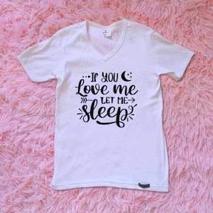 May include: White V-neck t-shirt with black text that reads "...If you love me let me sleep". The text includes a crescent moon and stars.