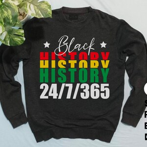 May include: A dark gray sweatshirt with the text "Black History 24/7/365" in white letters. The word "History" is repeated three times in red, yellow, and green.