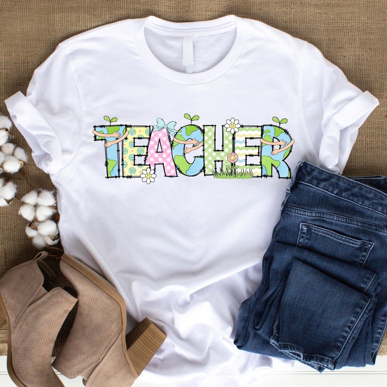 May include: White t-shirt with the word "TEACHER" in colorful patchwork letters. Each letter has a small green plant growing out of it and a small flower next to it.