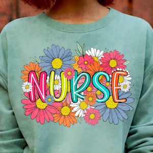 May include: A light green sweatshirt with a floral design and the word "NURSE" in colorful letters.