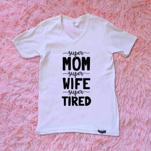 Op de afbeelding: Wit T-shirt met V-hals en zwarte tekst die "super mama super vrouw super moe" luidt.