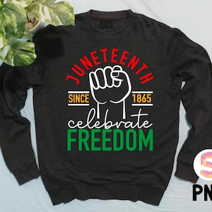 以下が含まれることがあります： 中央に握りこぶしのある、「Juneteenth Since 1865 Celebrate Freedom」という白いグラフィックデザインが施された黒いスウェットシャツです。