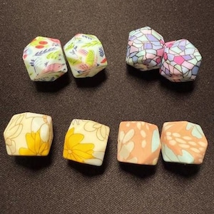 May include: An assortment of six-sided, geometric beads with various floral and abstract patterns. The beads feature colors like light blue, pink, yellow, and peach. Some beads have bird and flower designs, while others have mosaic-like patterns.