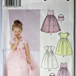 May include: Simplicity sewing pattern featuring a young girl in a pink dress with a matching purse. The pattern includes illustrations of several dress designs, including a pink dress, a green dress, and a checkered dress.