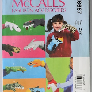 May include: McCall's M6667 Fashion Accessories sewing pattern envelope featuring illustrations of various animal-themed hand puppets. The designs include a white creature, a grey wolf, a leopard print animal, a shark, a monkey, a frog, an orange fish, and a blue bird. The pattern is labeled size OSZ.